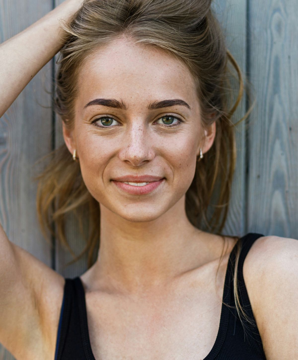 Smiling person with long hair against wooden backdrop.
